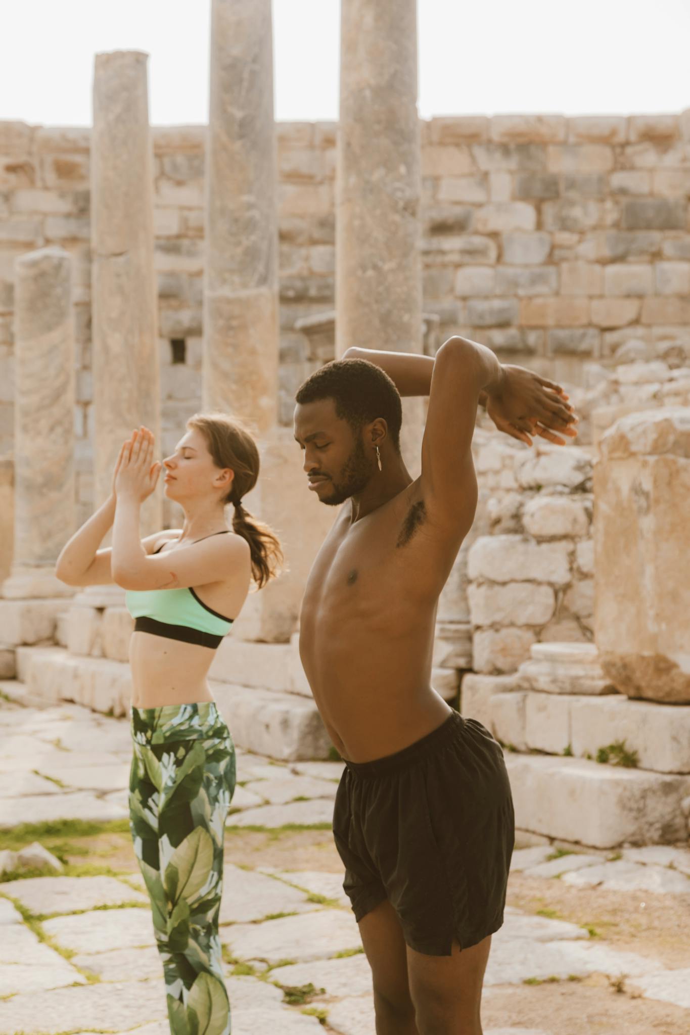 Diverse couple practicing yoga poses among ancient stone ruins on a sunny day.