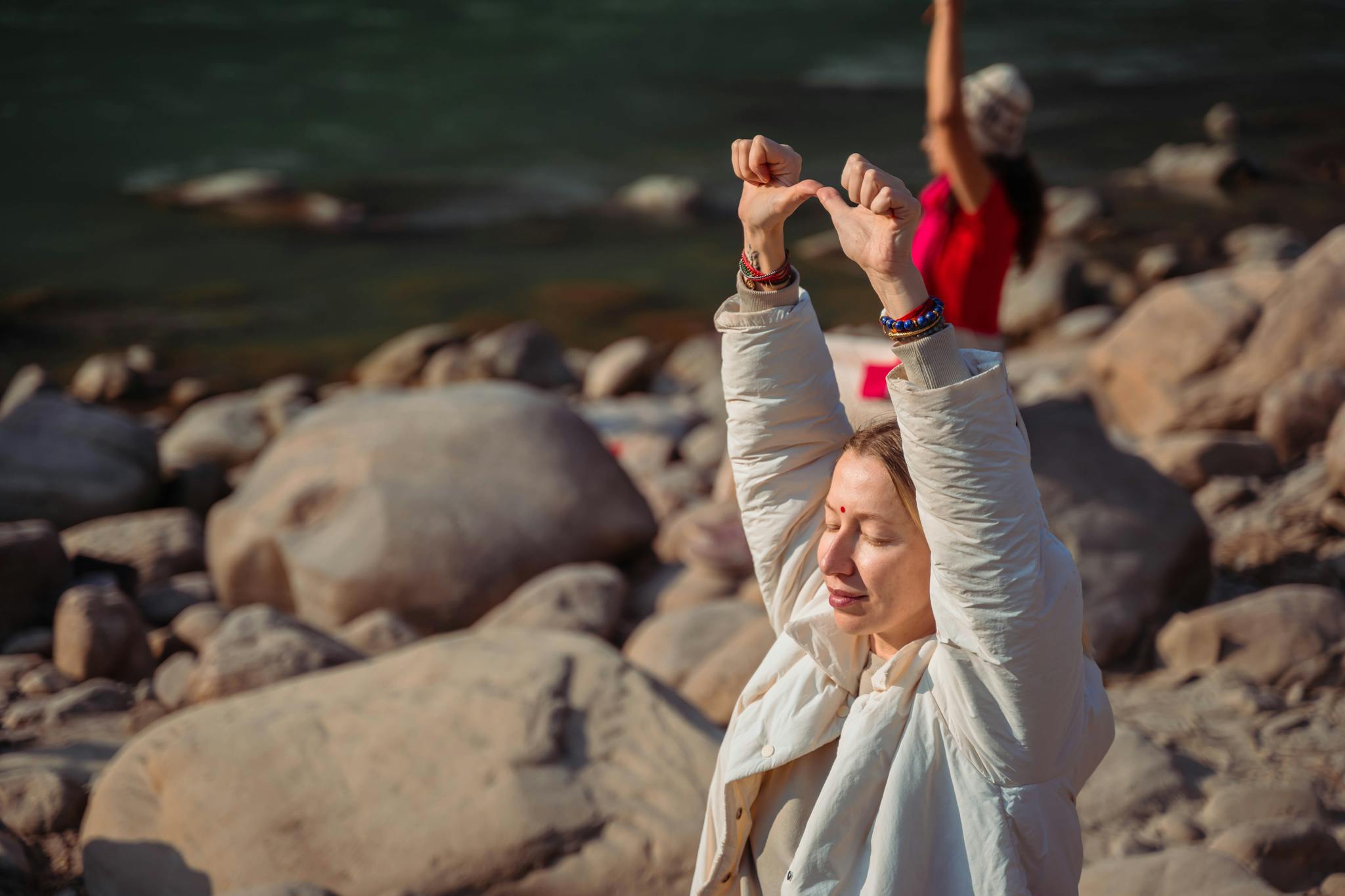 Relaxing by the Rishikesh river, a woman practices mindful meditation on rocky shores.